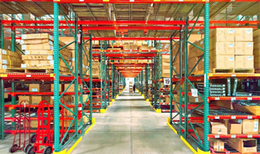 Allée centrale d’un entrepôt logistique avec des rayonnages remplis de cartons