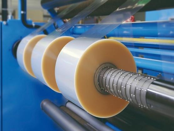 Rolls of plastic film being unwound on an industrial packaging production line.
