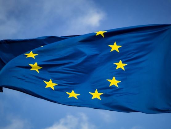 Blue European Union flag with twelve yellow stars arranged in a circle, waving in the sky.