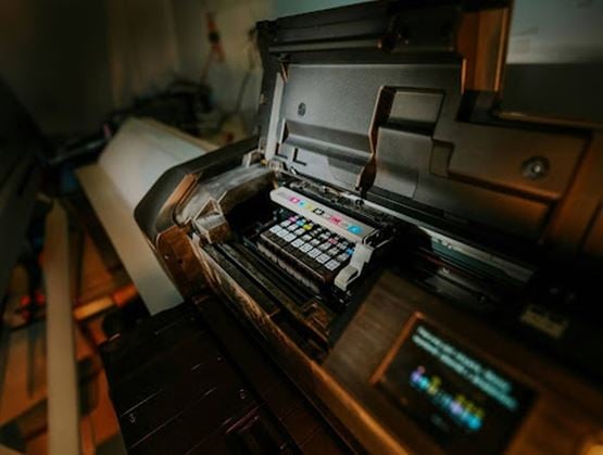 Professional printer with its cover open, revealing ink cartridges and internal printing mechanism in operation.