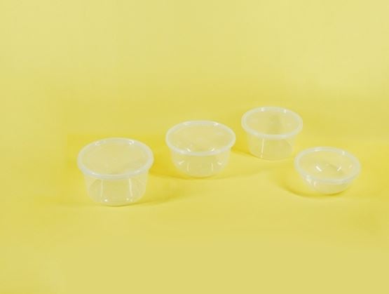 Quatre petits pots alimentaires transparents en plastique avec couvercle, disposés sur un fond jaune uni.