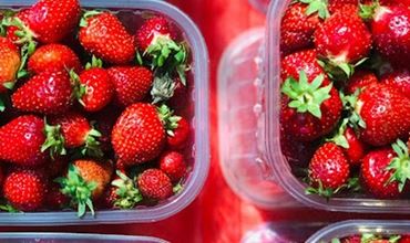Transparent containers filled with fresh red strawberries, placed side by side on a market display, with their green leaves still attached.