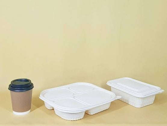 Cardboard coffee cup with a black lid and white compartmented fiber food containers placed on a plain beige background.