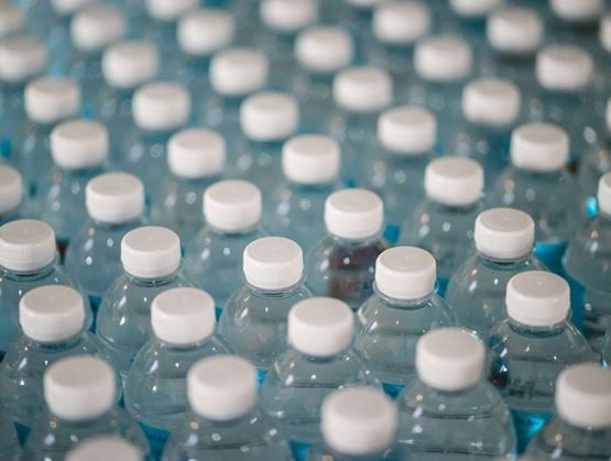 Rows of small clear plastic water bottles with white caps, filled with water and arranged in series on a bluish surface.