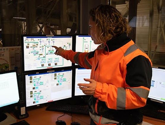 Operator in a wood processing factory monitoring and controlling an automated production line using multiple computer screens.