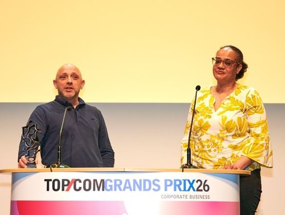 Two speakers on stage receiving a trophy during an awards ceremony, standing behind a podium at a professional event.