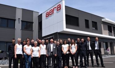Groupe de collaborateurs posant devant un bâtiment moderne portant l’enseigne Aera.
