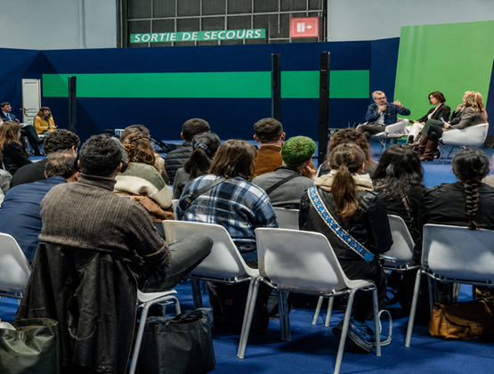 Public assistant à une table ronde avec plusieurs intervenants sur une scène lors d’un salon professionnel.