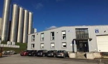 Bâtiment industriel avec plusieurs silos métalliques et des voitures stationnées devant.