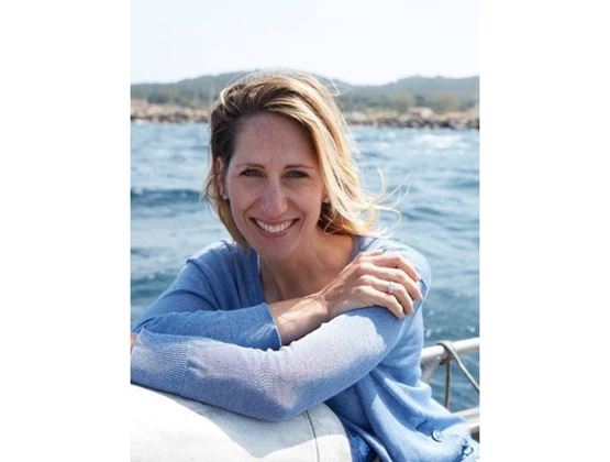 Portrait of a smiling woman in a blue sweater, sitting on a boat with the sea in the background.