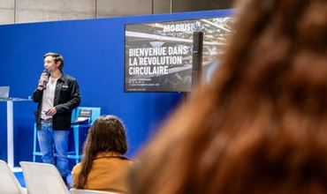 Un intervenant présente la révolution circulaire sur un stand bleu devant un public lors d’un salon professionnel.
