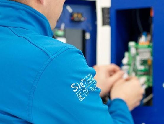 Technicien en veste bleue intervenant sur un équipement industriel électronique.