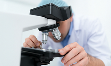 Scientifique en blouse et charlotte observant un échantillon au microscope en laboratoire.