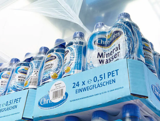 Packs of mineral water bottles wrapped in plastic film on an automated packaging line.