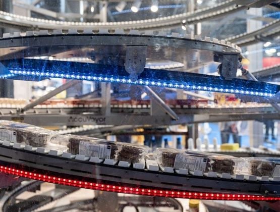Produits emballés circulant sur des convoyeurs industriels éclairés lors d’un salon professionnel.