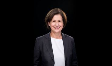 Portrait professionnel d’une femme souriante en veste sombre sur fond noir.