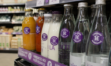 Bouteilles en verre réemployables présentées sur un rayon de supermarché avec des étiquettes de consigne à un euro.