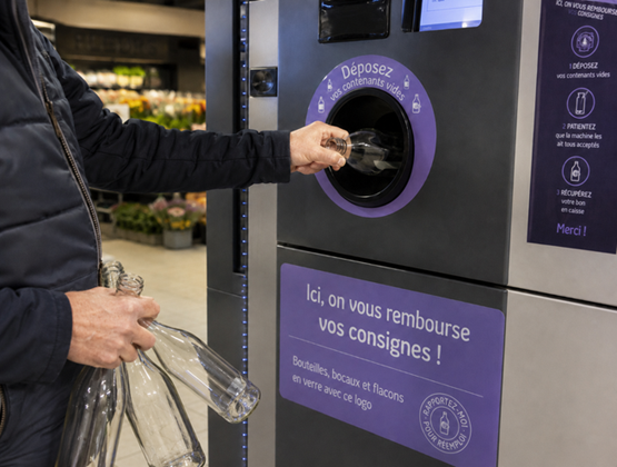Person inserting an empty glass bottle into a deposit return machine in a supermarket.