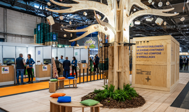 Wooden tree-shaped installation displayed at a packaging trade show, with booths, visitors and an eco-focused exhibition area.