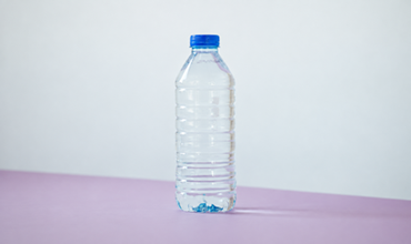 Clear plastic water bottle with a blue cap on a pastel surface.