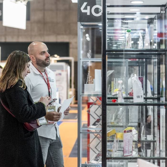 Two professionals are discussing around a table at a packaging solutions booth during a trade show.
