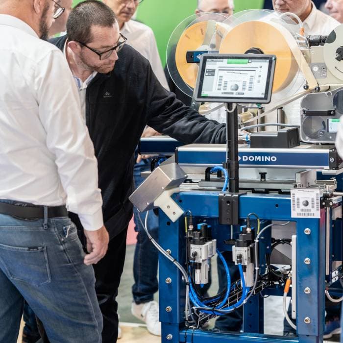 Visitors watch a demonstration of an industrial labeling machine at an exhibition booth.